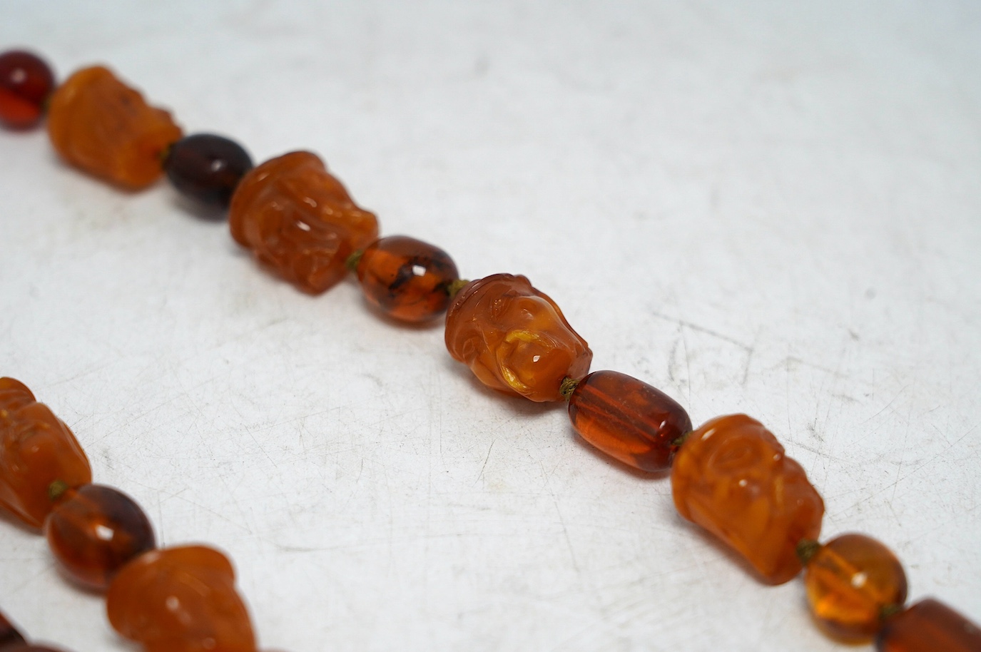 Two amber bead necklaces including Chinese with carved busts, 76cm and a pair of drop earrings, gross weight 145 grams. Condition - poor to fair